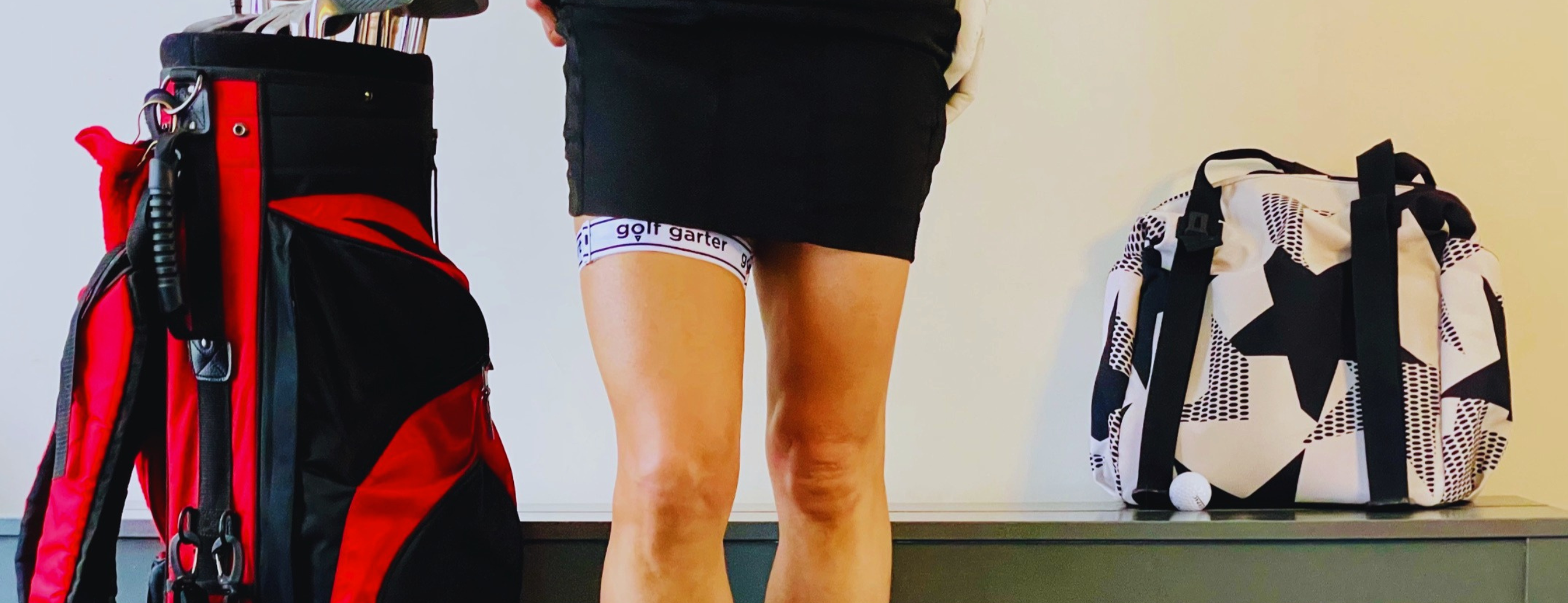 This is a photograph of women in a black skirt wearing a golf garter. There is a golf bag beside her one side. There is a gym bag and a golf ball beside her on the other side. 